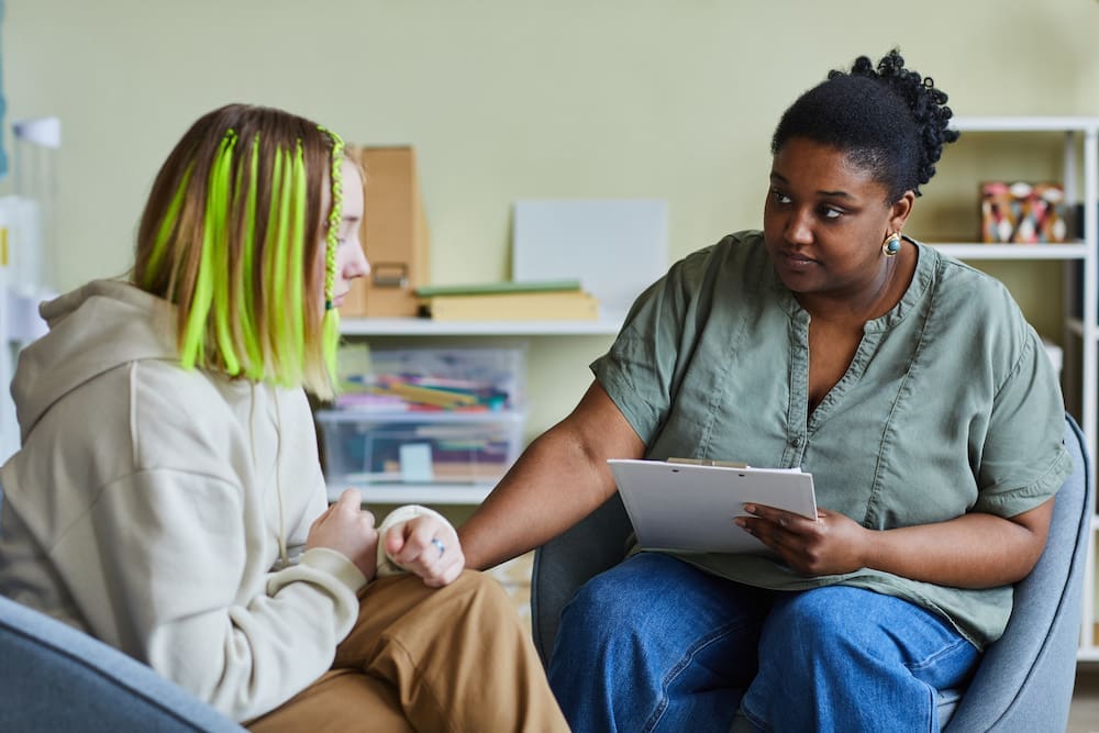 African female school psychologist supporting sad teenage girl during her difficult situation at school